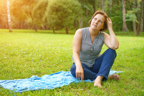 在一个阳光明媚的夏日，一位成年妇女坐在公园草地上的垫子上图片下载