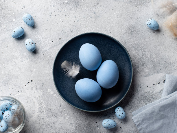 深蓝色的碗里放着蓝色的蛋和羽毛图片下载