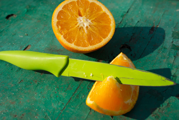 绿色的桌子上一片橙子，绿色的背景上一片橙子，刀在一张照片上一片橙子，刀切一个柑橘，绿色的刀在橙色的切片在绿色的板上，切片一个柑橘图片下载