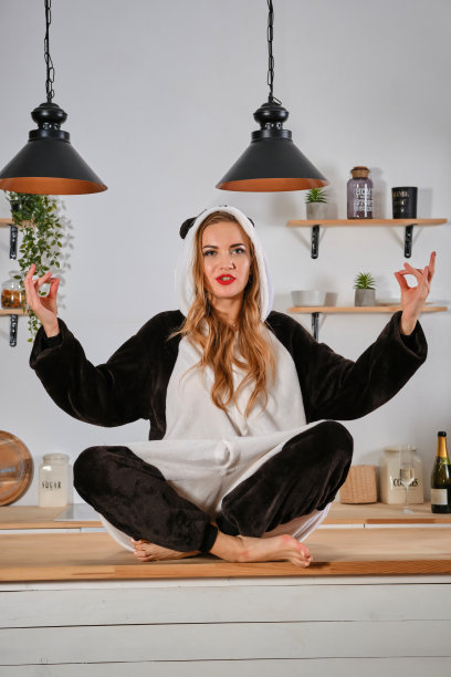 一名女子穿着毛绒睡衣，打扮成卡通人物熊猫的样子，在母鸡聚会上玩得很开心，坐在餐桌上摆着莲花姿势。特写镜头图片下载