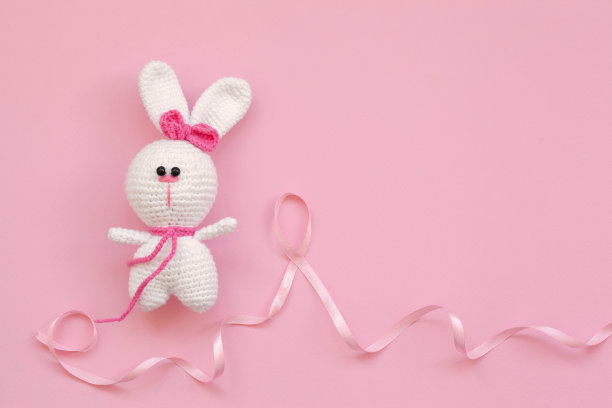 粉红色丝带乳腺癌与小针织婴儿玩具兔子在粉红色的背景。图片下载