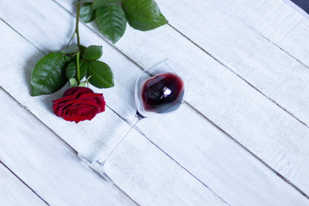 在白色的木质背景上放置红酒杯和勃艮第玫瑰与绿叶图片下载