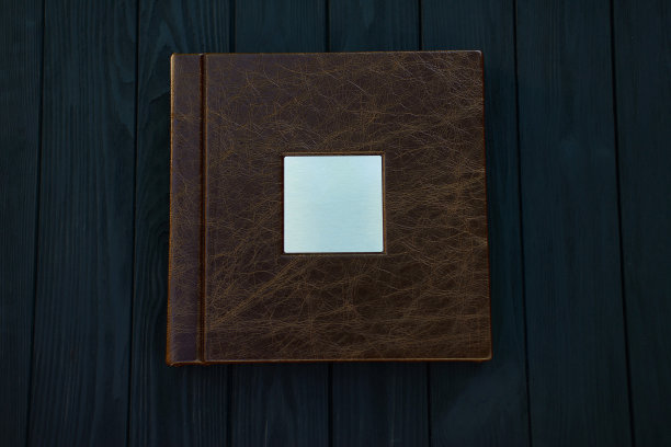 照片簿由真正的棕色皮革与金属银铭牌上的黑色木制背景。图片下载
