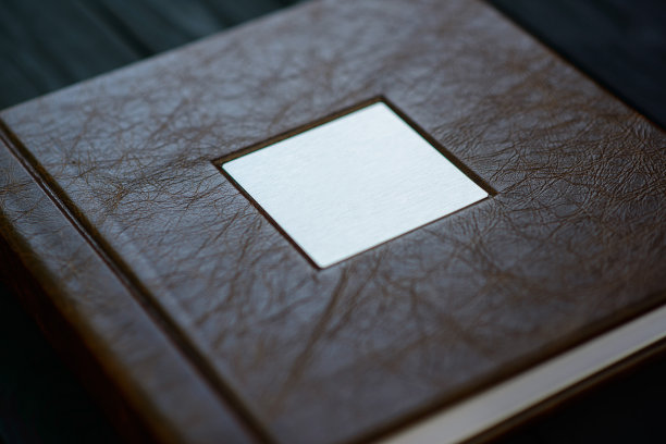 在黑色的木制背景上，用真正的棕色皮革制成的一本摄影集封面的纹理。图片下载