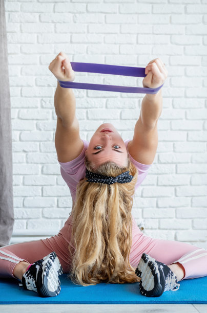 运动女性在家中白色砖墙背景的健身垫上使用阻力带进行锻炼图片下载