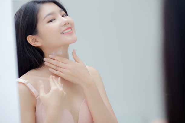 美丽的年轻亚洲女人照镜子，在颈部和信息上应用霜，美丽的女孩应用身体护理皮肤健康和柔软的水，治疗和化妆品与保湿。图片下载