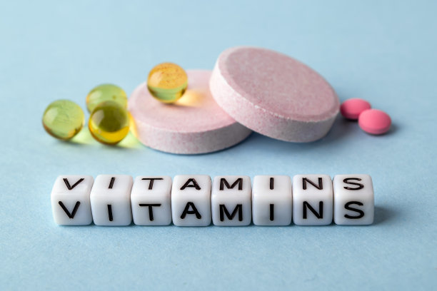 单词维他命由白色方块和不同的维他命组成，在蓝色医学背景上。生病，吃药或接受治疗的概念。卫生保健。图片下载