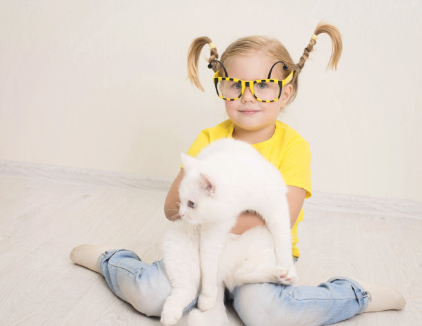 戴着蜜蜂眼镜、穿着黄色T恤、梳着辫子的小女孩开心地抱着她的猫，充满爱意。图片下载