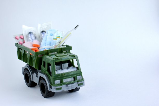 军用玩具车，装有药丸、医用口罩、注射器和安瓿，背景为光。人道主义援助的概念、卫生保健、药品短缺、出口。空间的文本。图片下载