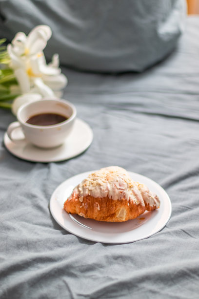 白玻璃盘上放着新鲜羊角面包，床上放着一杯咖啡。一束白色郁金香。早餐在床上。图片下载