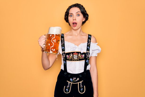 美丽的德国女人，蓝眼睛穿着传统的十月啤酒节的服装，喝着一罐啤酒吓在震惊与惊喜的脸，害怕和兴奋与恐惧的表情图片下载