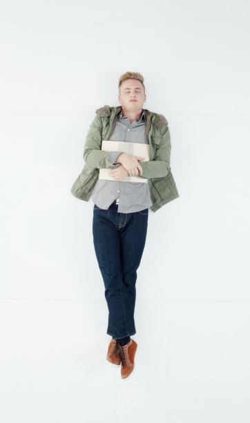 白人男学生躺在白色背景前，穿着牛仔裤，拿着书图片下载