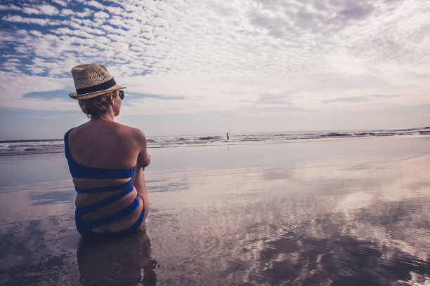 戴帽子的女人在海滩上看日落图片下载