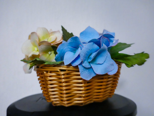 柳条篮子里的装饰花。柳条植物与人造花在白色和蓝色的家庭装饰。图片下载