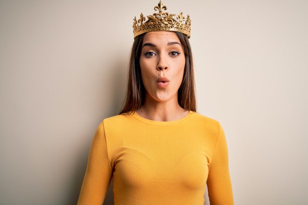 年轻美丽的黑发女人戴着金色的皇后皇冠在白色的背景害怕和震惊的表情，恐惧和兴奋的脸。图片下载