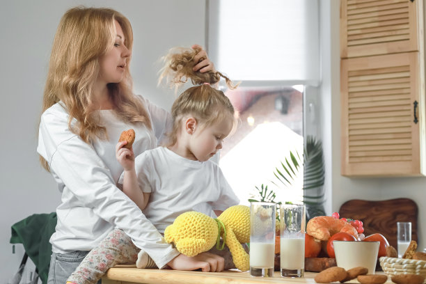 快乐的母女坐在厨房的餐桌旁，早上喝牛奶，愉快地交谈。在明亮的厨房里享受维生素早餐的照片图片下载
