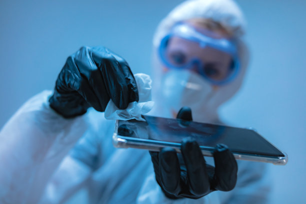 医生身穿防护服手持消毒湿巾为智能手机消毒图片下载