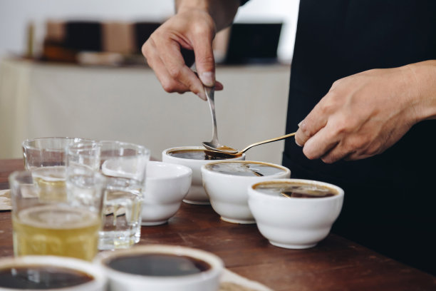 专业的Q分级师准备测试和检查咖啡的质量，并从桌上的陶瓷杯上撇去咖啡渣。电影风格的照片。图片下载