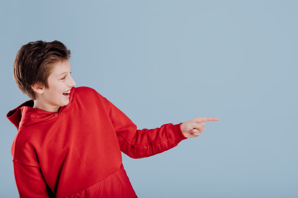 快乐的学生在红色运动衫指向指向在工作室的方向上的蓝色背景，侧面视图图片下载
