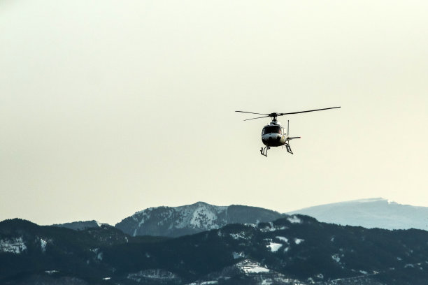 一幅大气图片显示直升飞机在高耸的雪山前攀登。图片下载