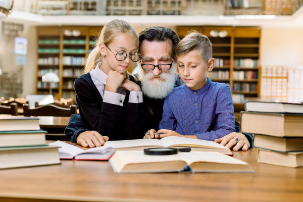 快乐的大胡子老人，爷爷和他可爱的孙子孙女坐在古老的图书馆的桌子旁看书。家庭休闲，读书，读书图片下载