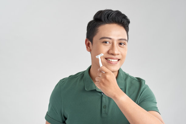 一名亚洲男子站在白色背景上，手里拿着剃须刀刮胡子。男性保健的概念。图片下载