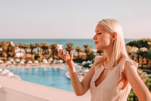 在街上看着小化妆镜检查妆容的金发迷人年轻女人图片下载