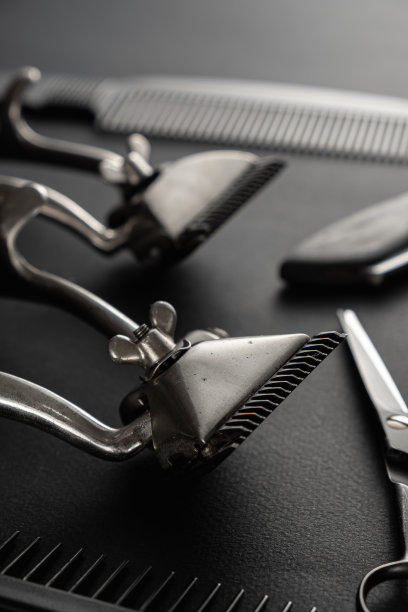 在黑色的表面上是旧的理发工具。两个老式手动理发器，梳子，剃须刀，剃须刷，美发剪刀。黑色的单色。垂直图片下载
