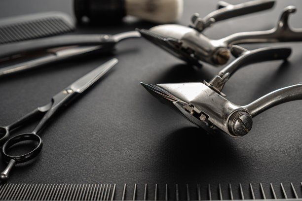 在黑色的表面上是旧的理发工具。两个老式手动理发器，梳子，剃须刀，剃须刷，美发剪刀。黑色的单色。图片下载