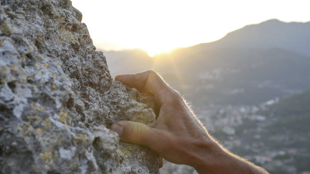 日出时，双手紧握岩石脊上的岩石图片下载