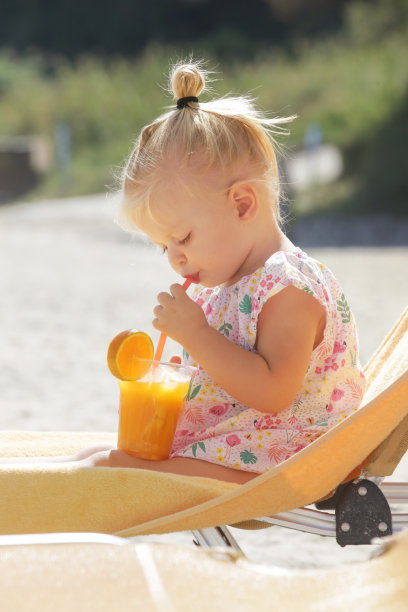 坐在躺椅上喝橙汁的可爱金发幼儿图片下载