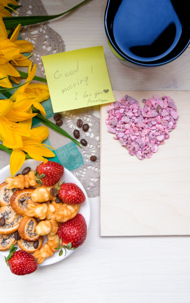 情人节心形草莓饼干配咖啡，餐巾纸上有黄花，笔记本上有笔，便条上有文字“早上好，我爱你”图片下载