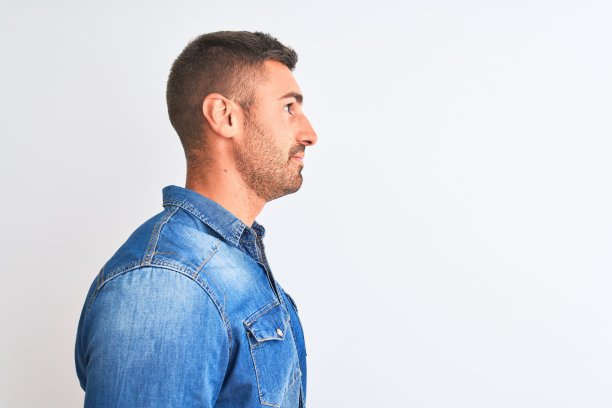 年轻英俊的男子穿着牛仔夹克站在孤立的背景看向一边，放松的侧面姿势与自然的脸与自信的微笑。图片下载