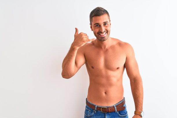 年轻英俊的赤膊男子显示肌肉的身体在孤立的背景微笑做电话手势与手和手指，就像在打电话。沟通的概念。图片下载