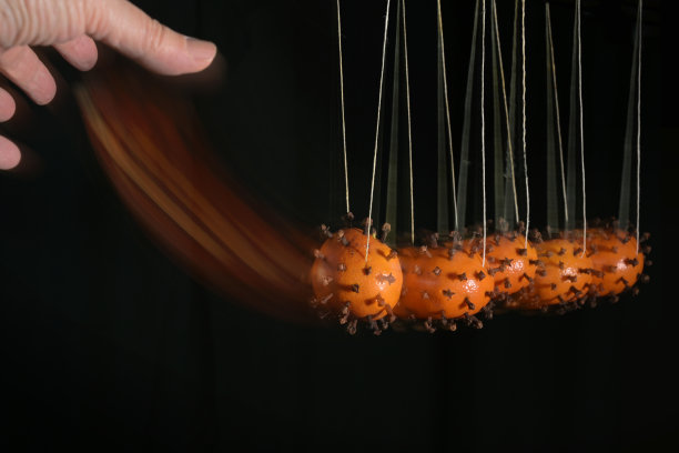 汉德正在移动带有冠状病毒模型的牛顿摇篮，该模型由橘子和丁香混合制成，以说明感染是如何通过接触传播的，运动模糊，黑色背景和复制空间图片下载