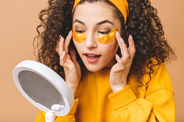 年轻纯洁美丽的卷发女人的形象孤立的米色背景照顾她的皮肤与眼罩。图片下载