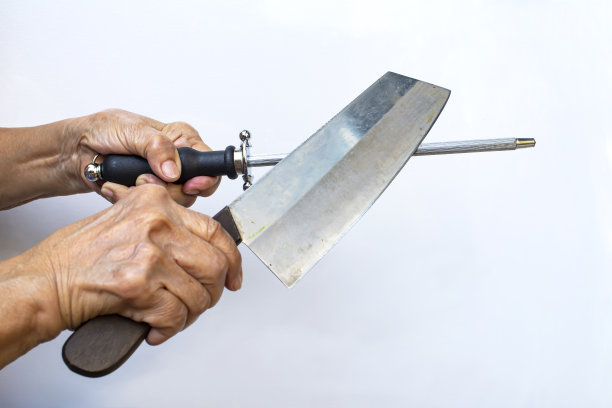 高级女性手持磨刀机在白色背景上磨刀，近距离拍摄，选择性聚焦，厨房用具概念图片下载