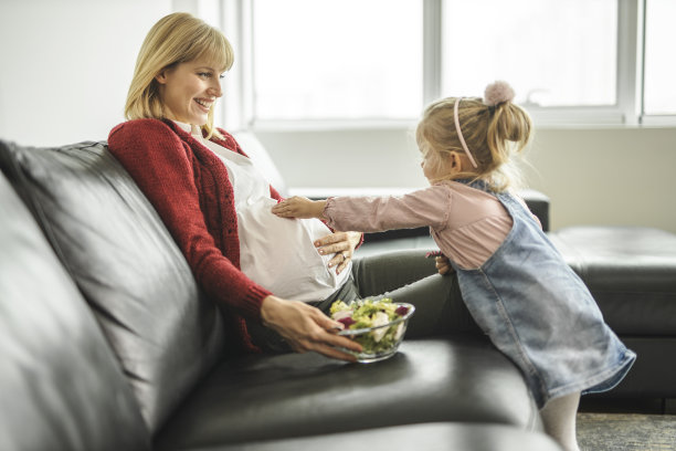 怀孕的母亲和女儿吃着健康的沙拉，在家里的客厅里玩耍图片下载