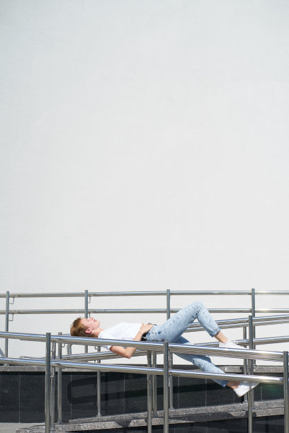 红发短发年轻女人在炎热夏日里躺在城市中心的栏杆上图片下载