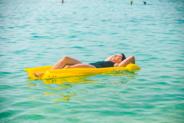 在海水中躺在黄色充气床垫上的美丽女人图片下载