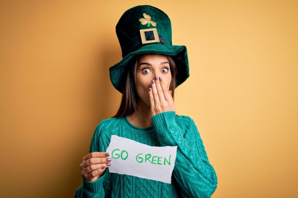 年轻美丽的女子戴着绿帽子庆祝圣帕特里克节，手持短信捂着嘴，因错误而震惊，表情恐惧，默默害怕，秘密概念图片下载