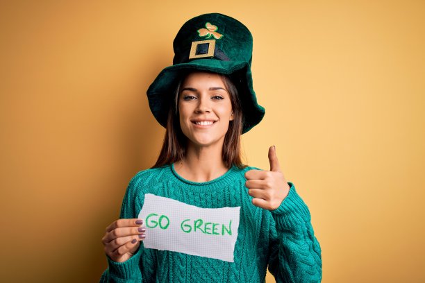 年轻美丽的女人戴着绿帽子庆祝圣帕特里克节，带着大大的微笑做ok手势，大拇指向上的手指，优秀的手势图片下载
