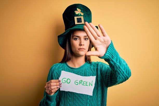 年轻美丽的女人戴着绿色的帽子庆祝圣帕特里克节的信息与开放的手做停止标志与严肃和自信的表情，防御手势图片下载