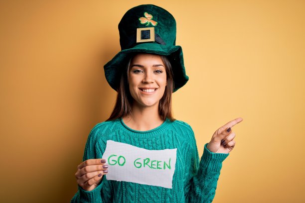 年轻美丽的女子戴着绿帽子庆祝圣帕特里克节，手里拿着祝福语非常幸福地用手指向一边图片下载