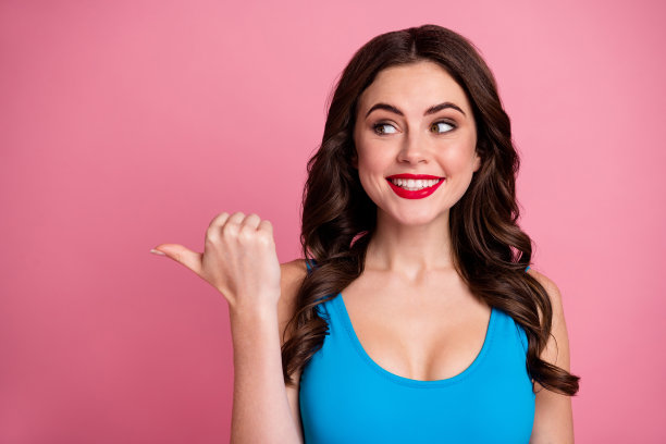 疯狂滑稽的卷发女士的特写照片直接拇指手指侧空白显示低价广告横幅销售报价穿休闲的蓝色背心孤立的粉红色背景图片下载