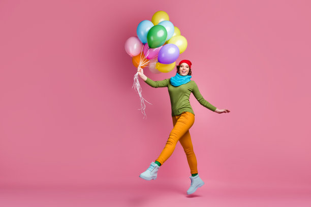 丰满的照片，快乐的漂亮的女孩跳，抱着许多气球，她在节日得到享受秋天自由时间穿套头衫，红色的头饰，裤子孤立的粉色背景图片下载