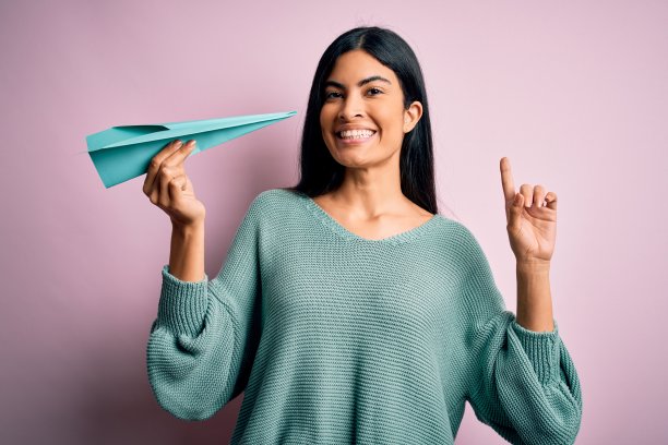 年轻美丽的西班牙妇女拿着纸飞机和通信和旅行信息惊讶与一个想法或问题指向幸福的脸手指，第一图片下载