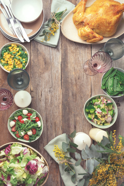 节日家庭餐桌。提供盘子，碗与沙拉和蔬菜菜肴，零食，整个烤鸡，桉树，含苞欲放的花木制背景。情人节，妇女节，母亲节图片下载