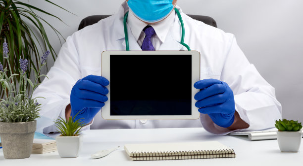 男医生穿着白大褂坐在办公桌前，手里拿着一个黑屏的电子平板电脑图片下载