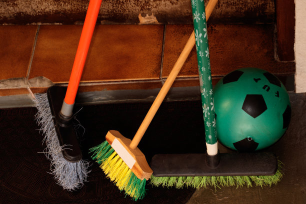 三把扫帚，一把给孩子的，还有一个绿色的球，放在一扇木门前。图片下载